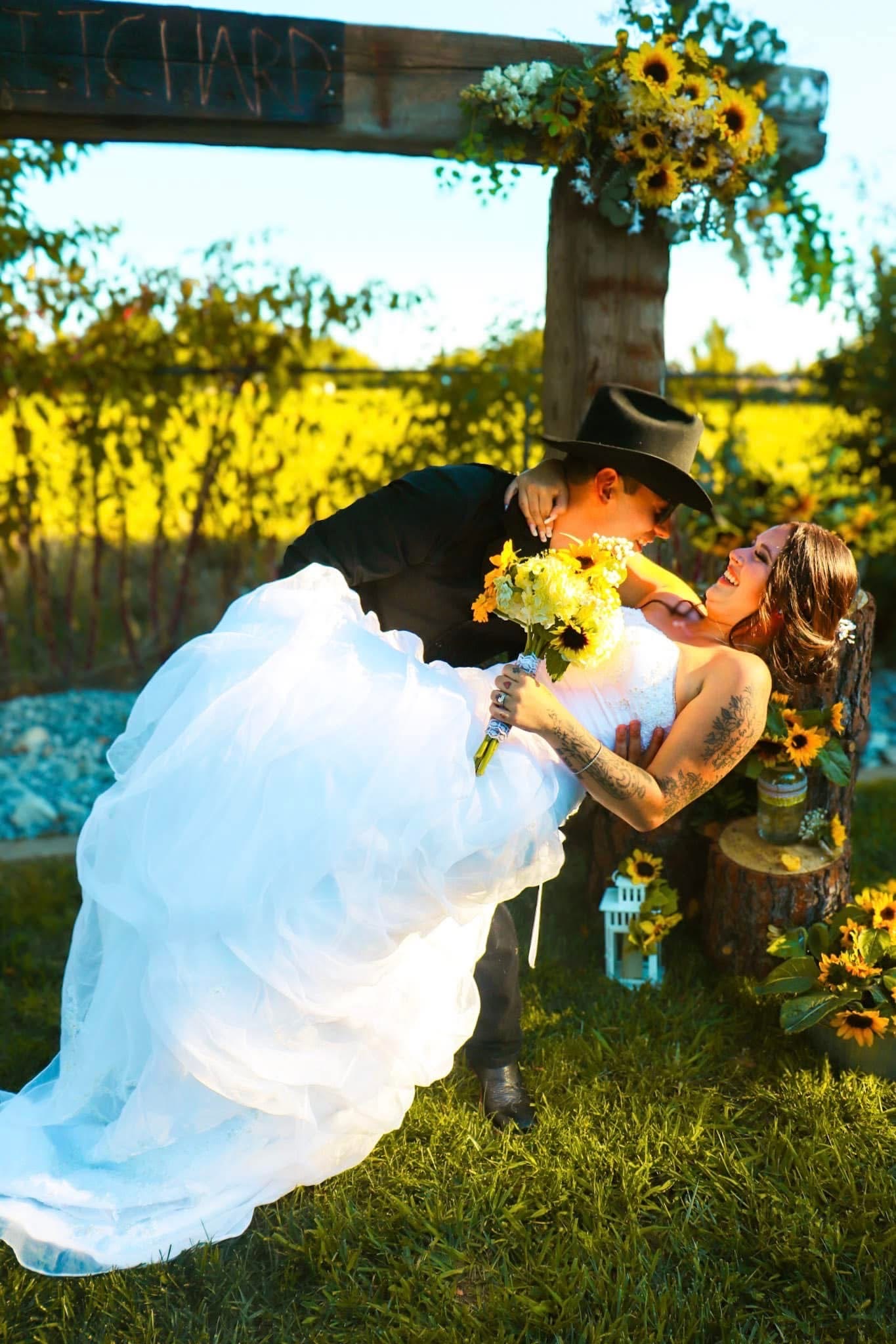 Sam dipping Meriah beneath the sunflower wedding arch on their wedding day